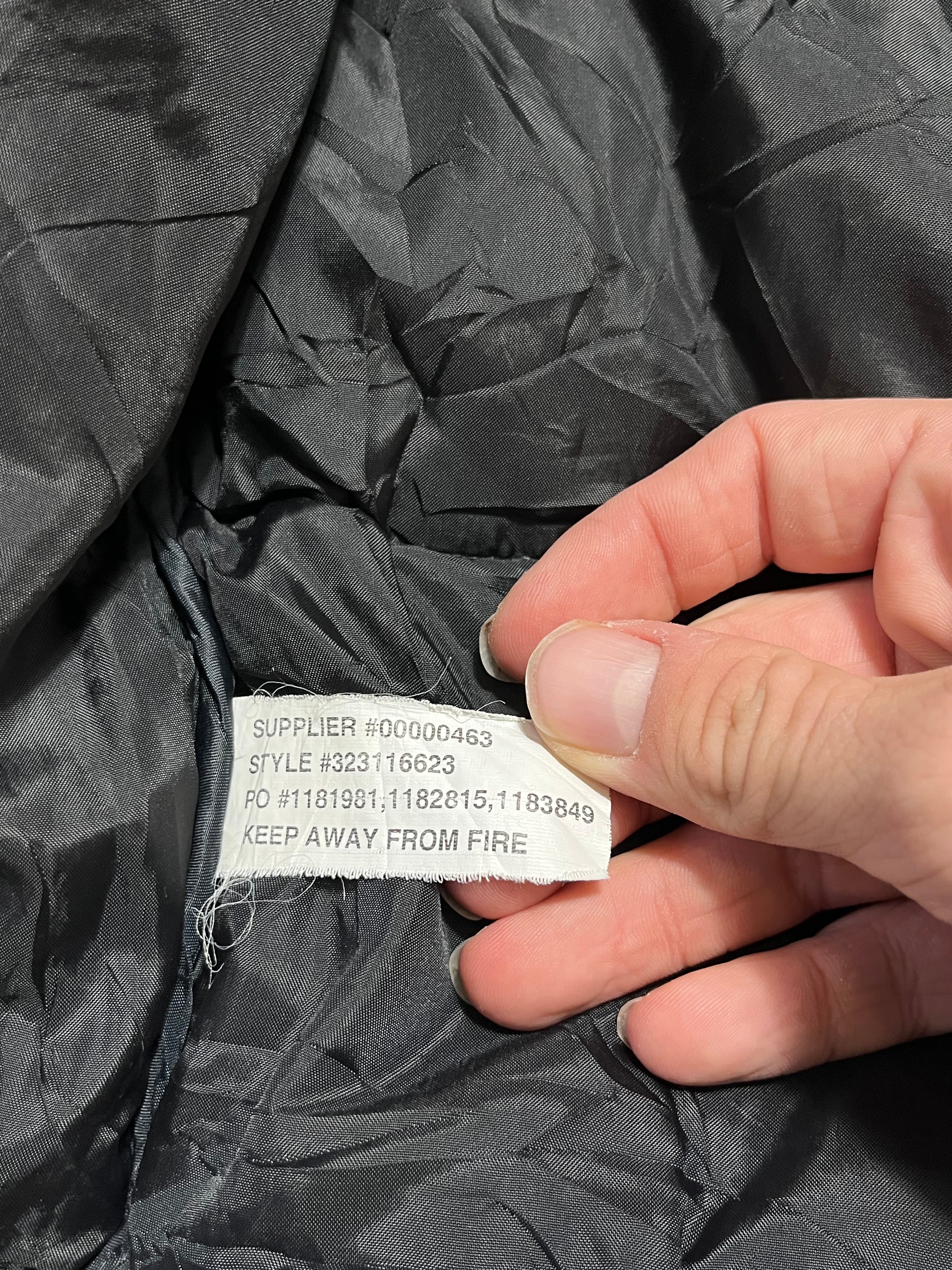 Fekete streetwear dzseki belső címke, kézzel tartva, stílus- és cikkszámmal.