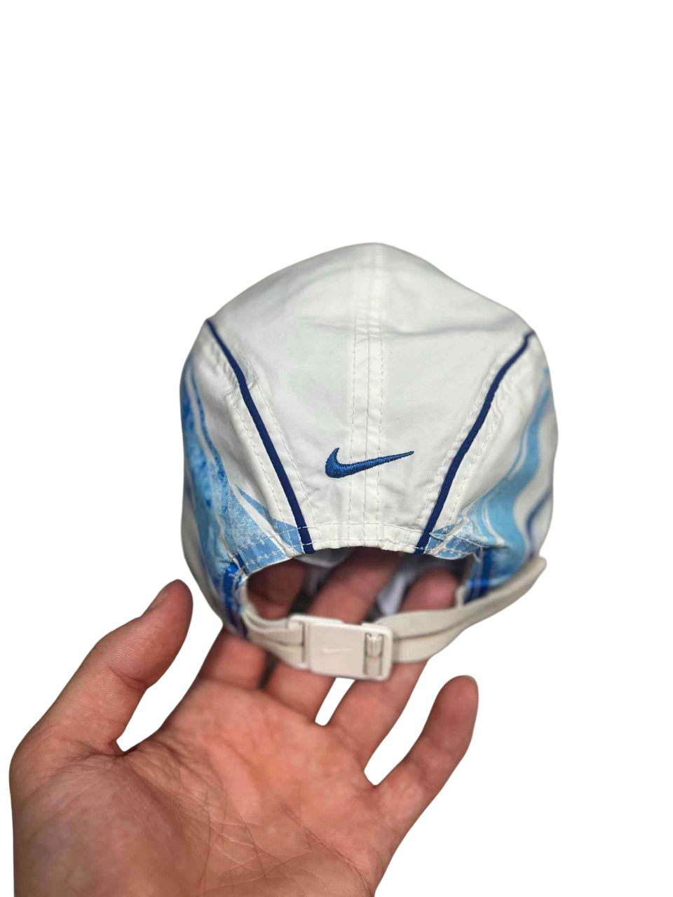 Fehér vintage Nike sapka kék mintával, állítható pánttal, kézben tartva, streetwear stílus