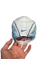 Fehér vintage Nike sapka kék mintával, állítható pánttal, kézben tartva, streetwear stílus