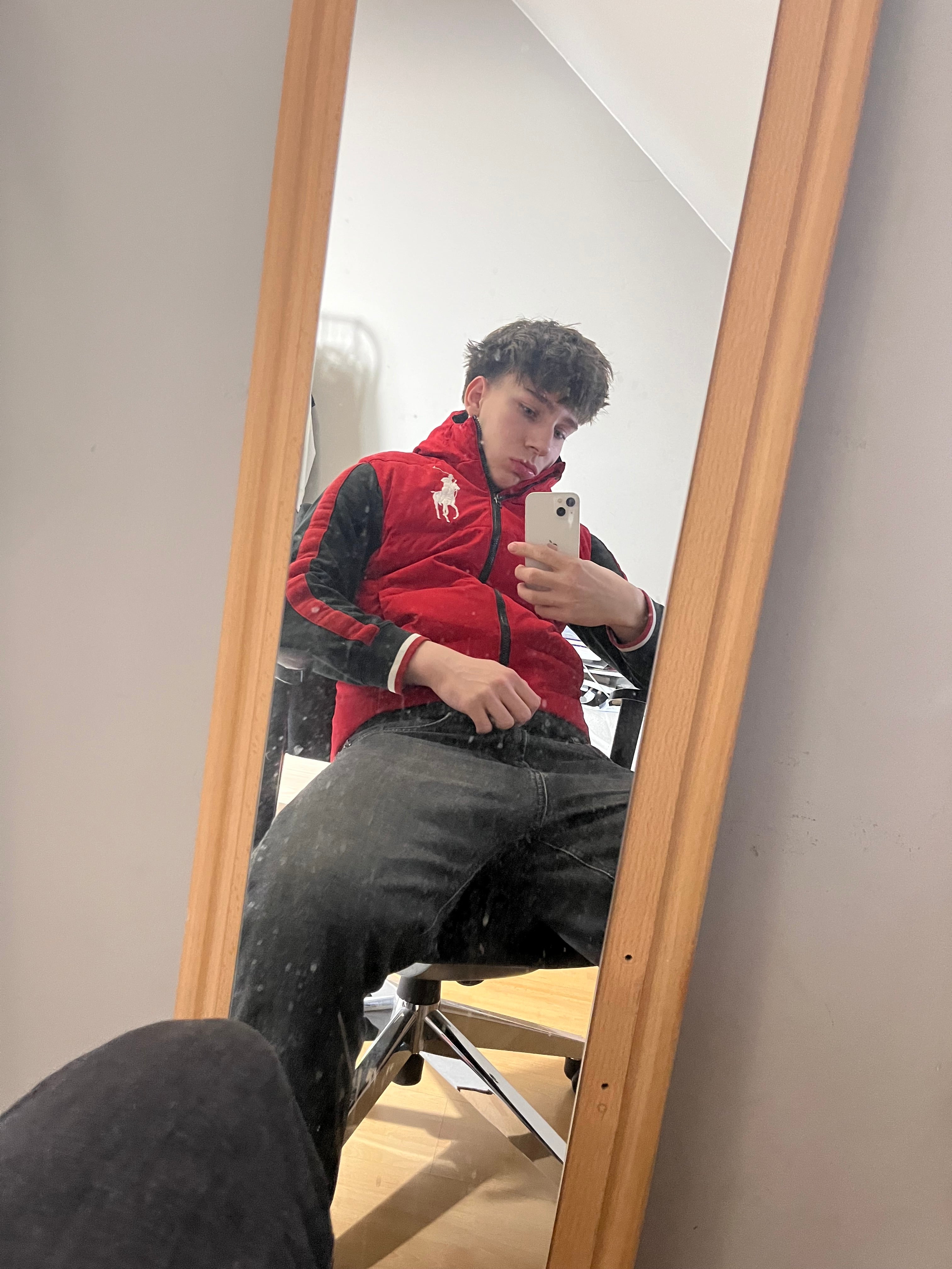 Fiatal férfi tükörszelfi piros Ralph Lauren streetwear mellényben, farmernadrágban, modern enteriőrben.